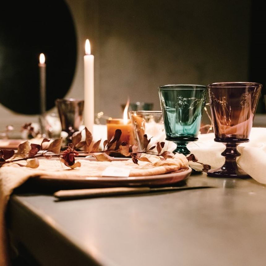 Decorative table setting with candles and colored glassware on a dark surface.