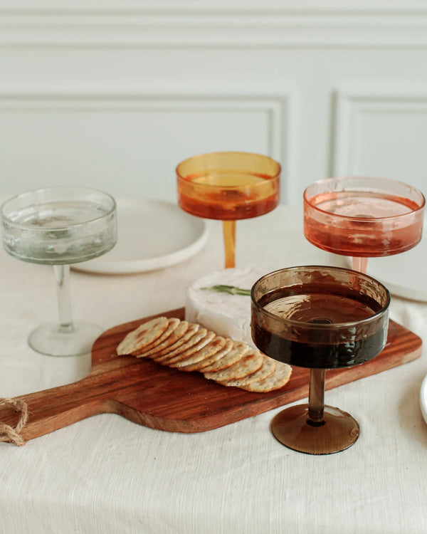 Cocktail glasses with different colored liquids on a wooden board with crackers.