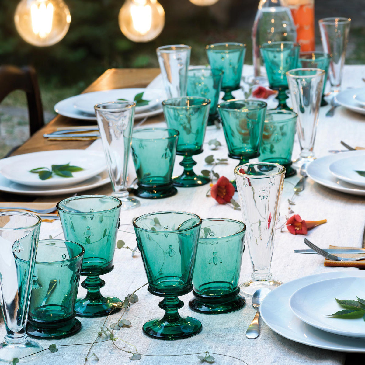 Table setting with green glassware and white plates outdoors.