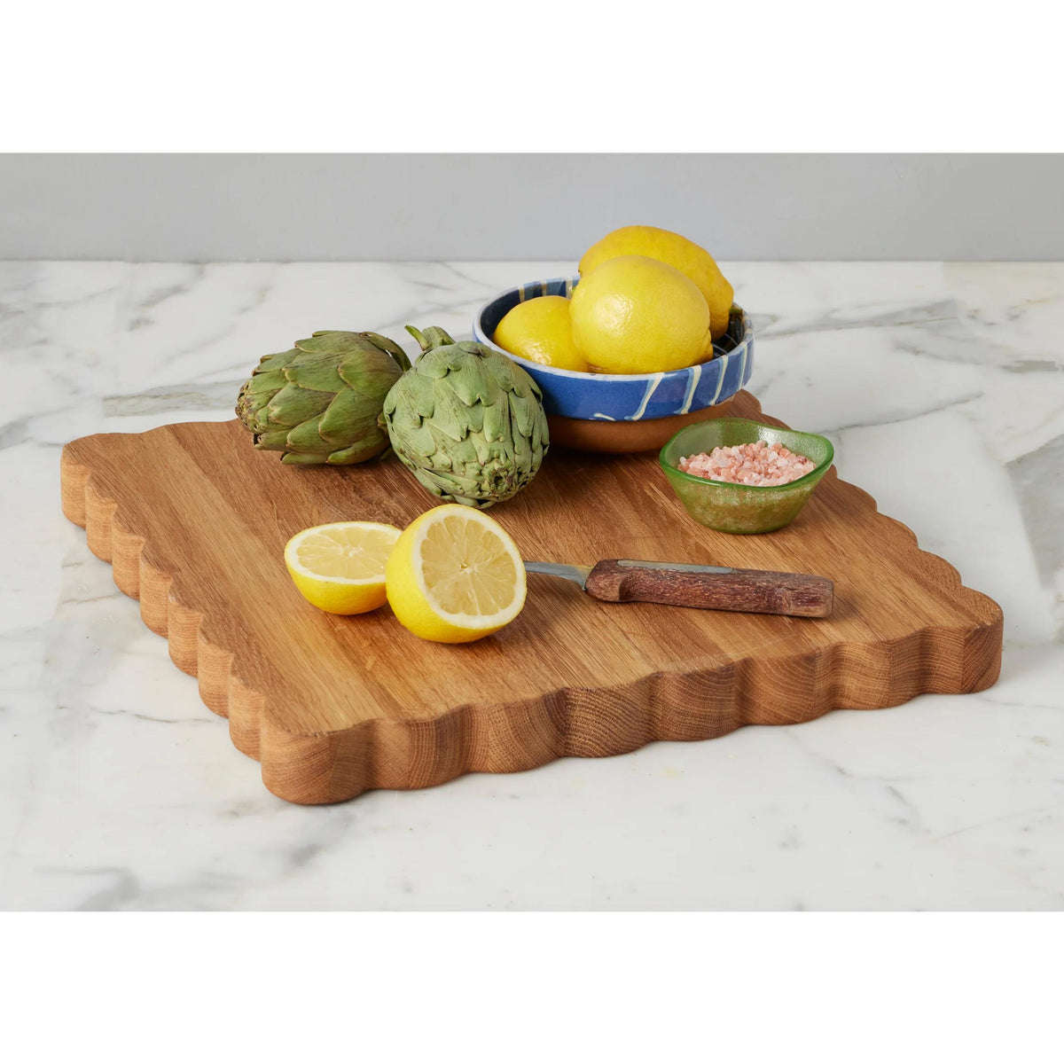 Acacia wood scalloped cutting board with lemons, artichokes, and pink salt.