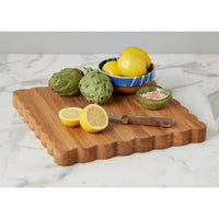 Acacia wood scalloped cutting board with lemons, artichokes, and pink salt.