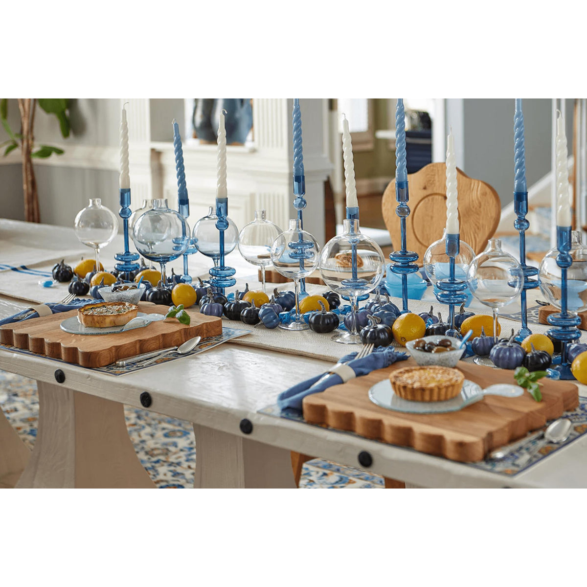 Acacia wood scalloped cutting boards on a dining table with blue candles and decorative gourds.