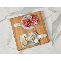 Square acacia wood scalloped cutting board with two grey serving boards holding charcuterie and cheese.