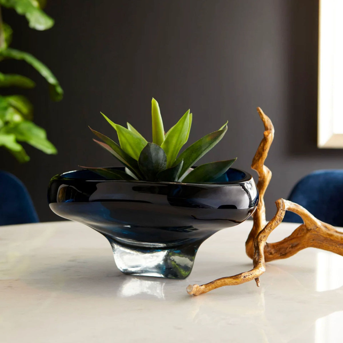 Small cobalt blue glass decorative bowl with an abstract design, holding a green succulent on a white marble table.