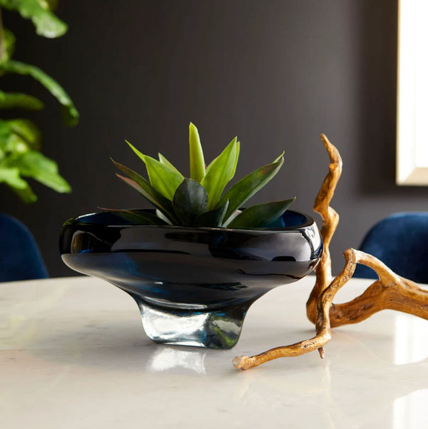 Small cobalt blue glass decorative bowl with an abstract design, holding a green succulent on a white marble table.