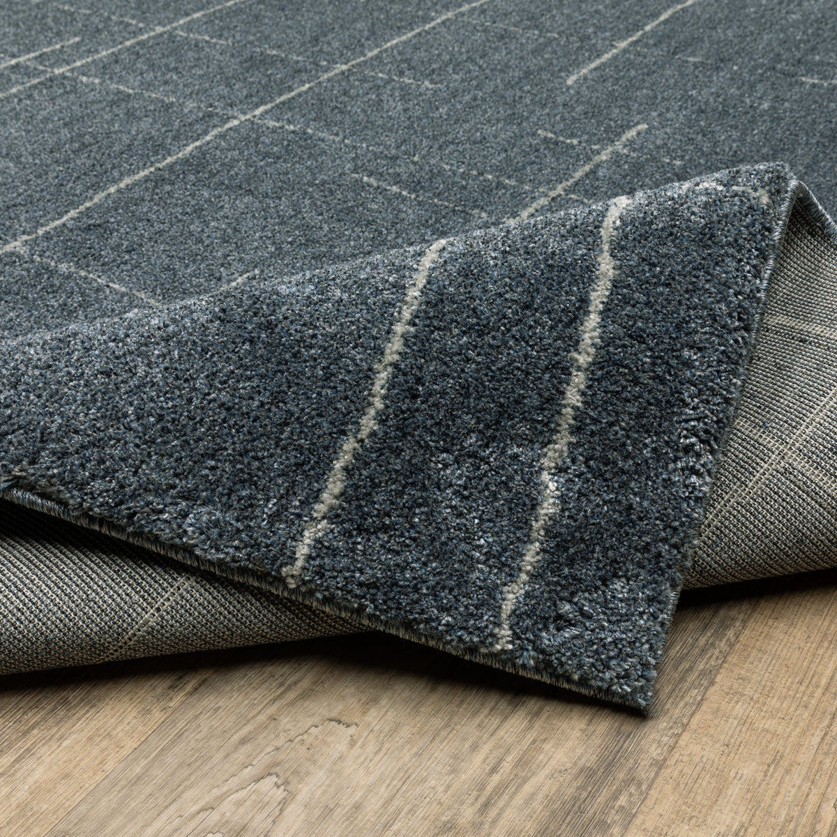 Alton Blue & Beige casual rug, power-loomed polyester with subtle grid pattern, partially rolled on wood floor.