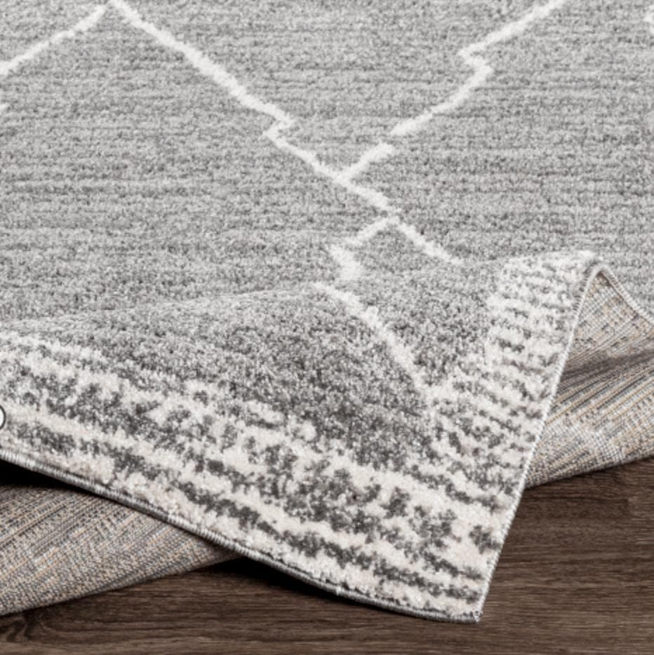 Andorra Charcoal & White polypropylene rug with a globally inspired geometric design, partially rolled on a wood floor.