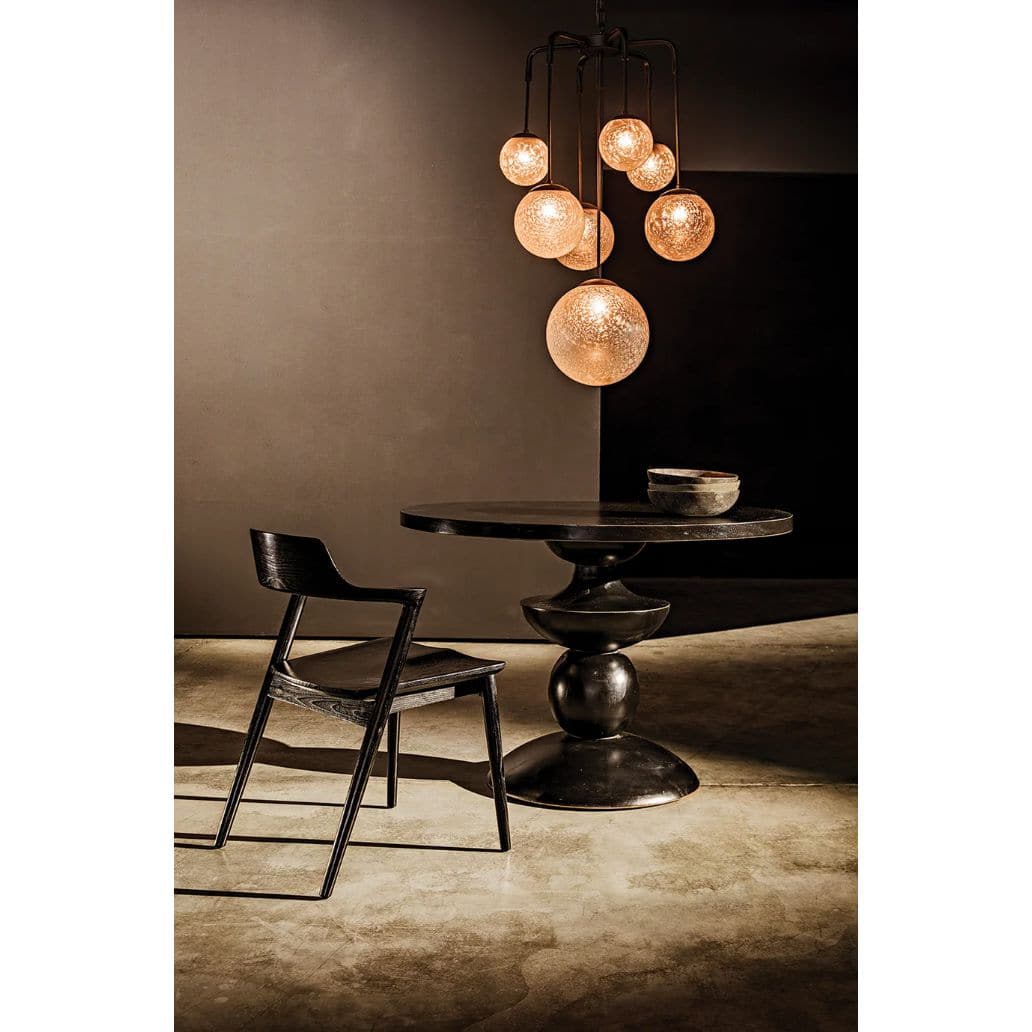 Artemis Chandelier with seven handblown glass bubbles and black steel arms over a dark table and chair.
