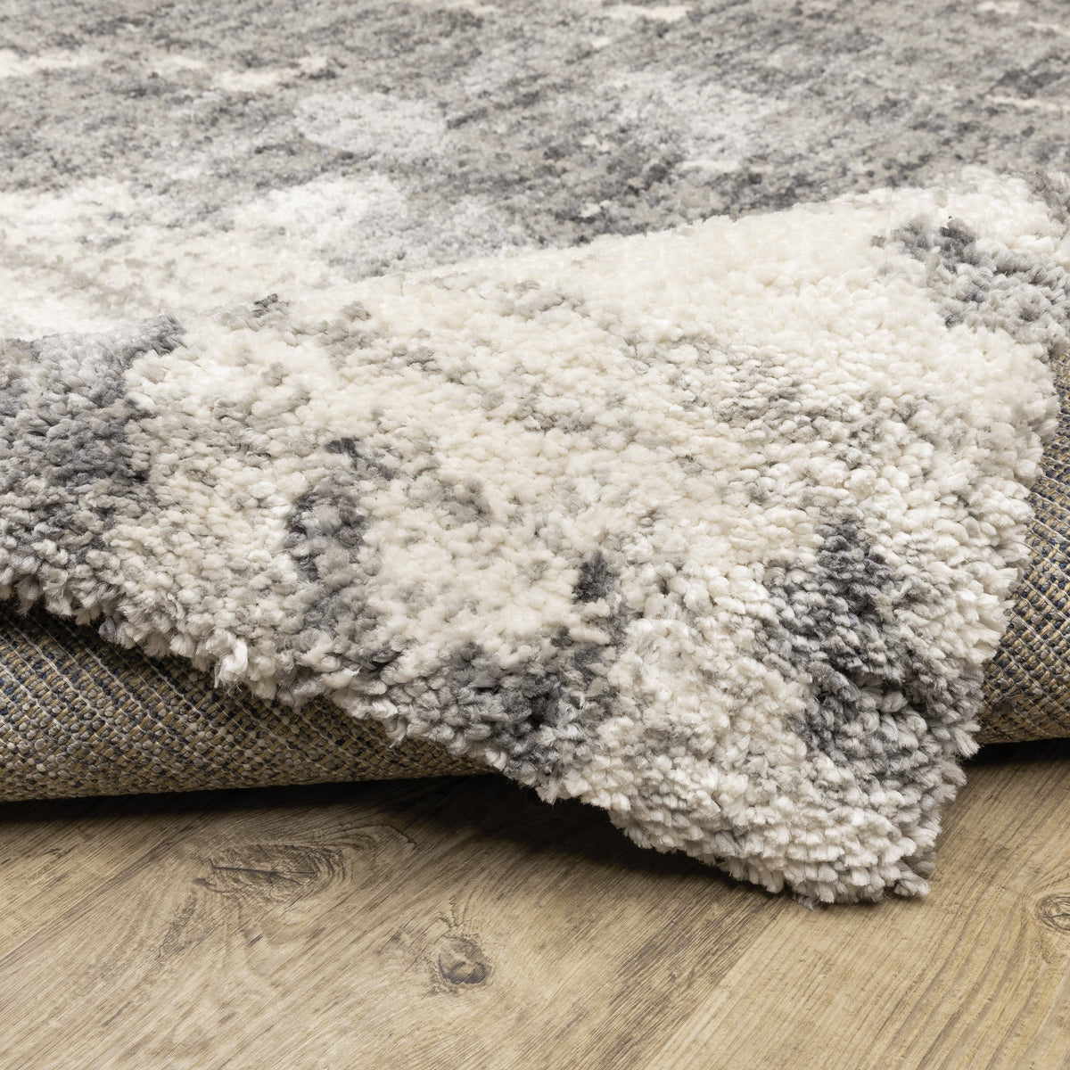 Close-up of an Aspen Grey & Ivory Contemporary Rug, showing its soft, textured microfiber polyester pile and woven backing on a wood floor.