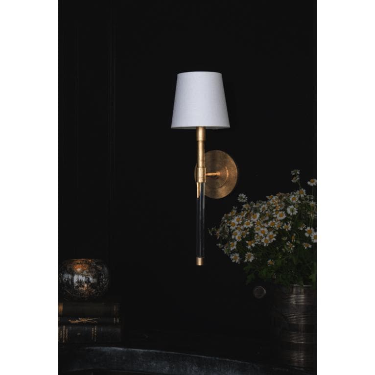 Auburn brass and crystal sconce with a white linen shade on a dark wall.