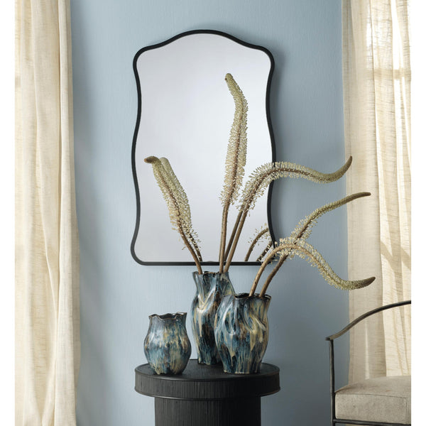 Aurora Wavy Wall Mirror with a thin black metal frame and unique waved edge, hung vertically above three decorative vases.