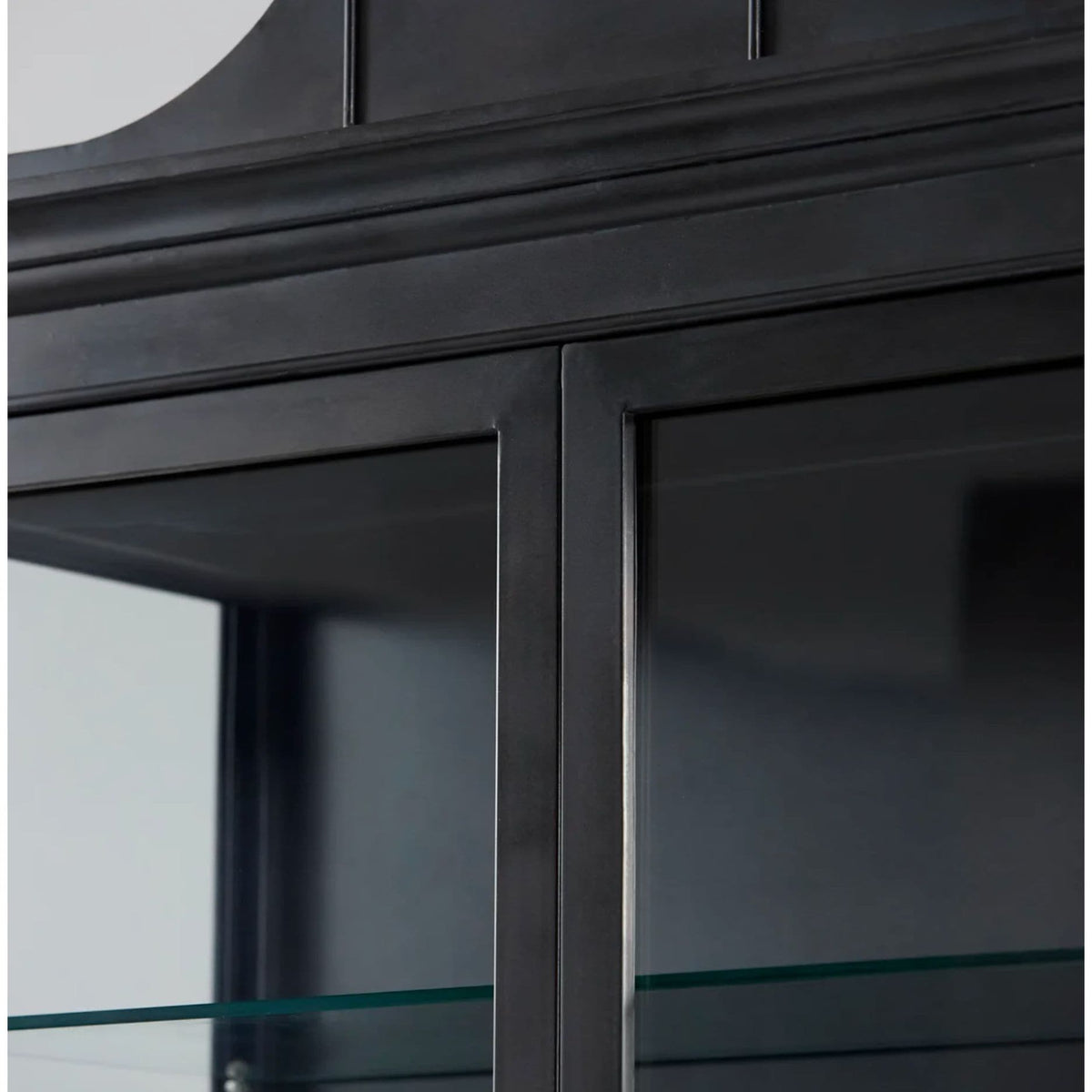 Black iron curio cabinet with glass doors, decorative molding, and internal glass shelves.