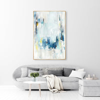 Abstract giclee canvas painting with blue, white, and yellow strokes in a gold frame above a gray sofa.