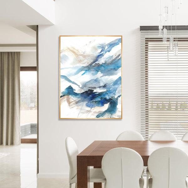 Abstract giclee canvas painting with blue, white, and gold brushstrokes in a gold frame, hanging above a wooden dining table.