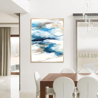 Abstract blue and white giclee canvas painting with brush gel finish in a gold frame, hanging in a modern dining room.