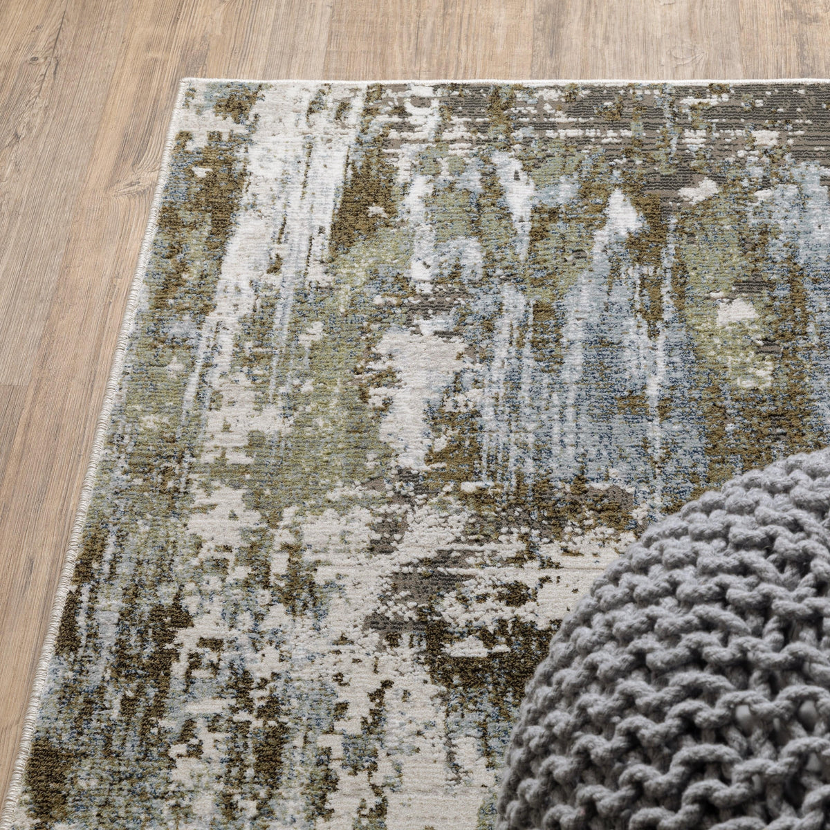 Caravan Moss Green & Blue Contemporary Rug with textured, multi-level surface and a gray knitted pouf.