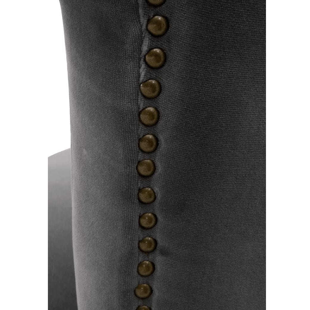Close-up of a Celina Dark Dove velvet dining chair, showing the dark gray upholstery and decorative brass nailhead trim.