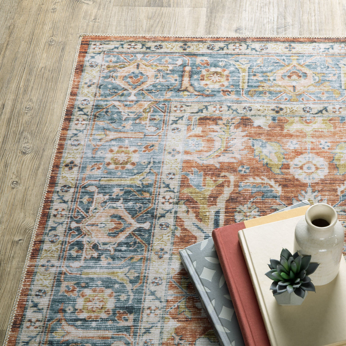 Charleston Rust & Blue Washable Rug with distressed traditional patterns on a wood floor, styled with books and decor.