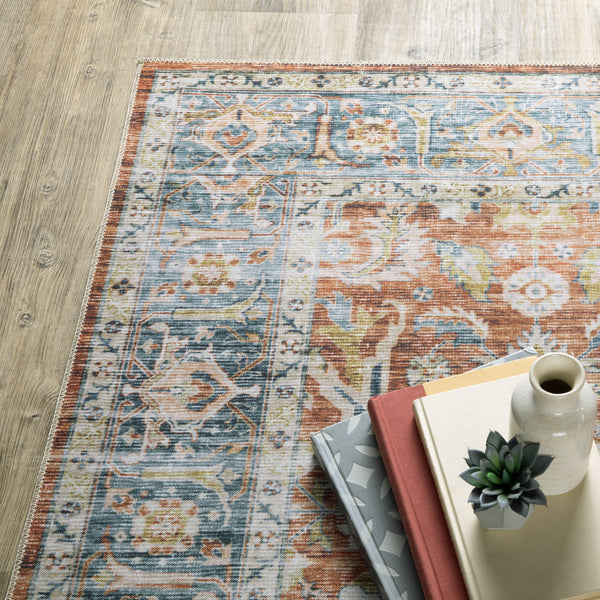 Charleston Rust & Blue Washable Rug with distressed traditional patterns on a wood floor, styled with books and decor.