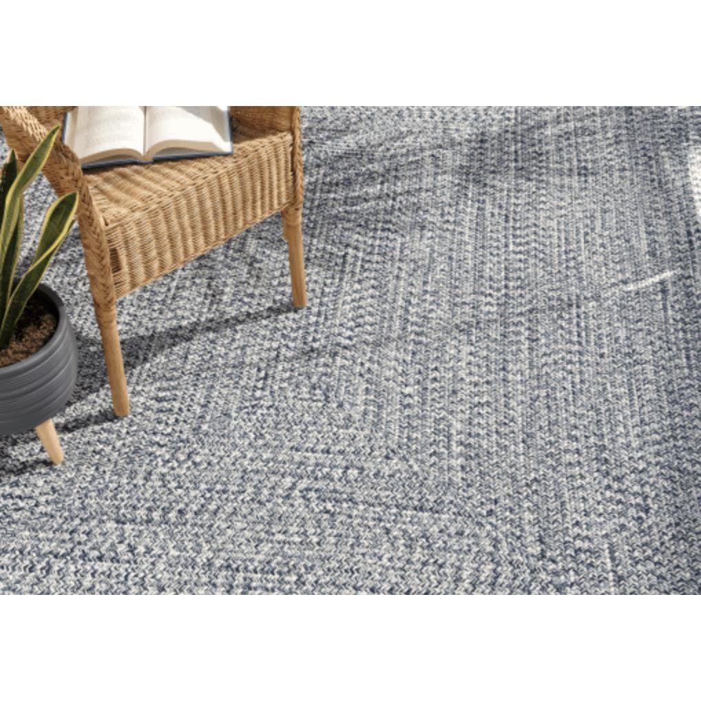 Chesapeake Bay blue and cream braided polypropylene outdoor rug with a wicker chair and plant.