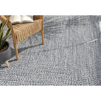 Chesapeake Bay blue and cream braided polypropylene outdoor rug with a wicker chair and plant.