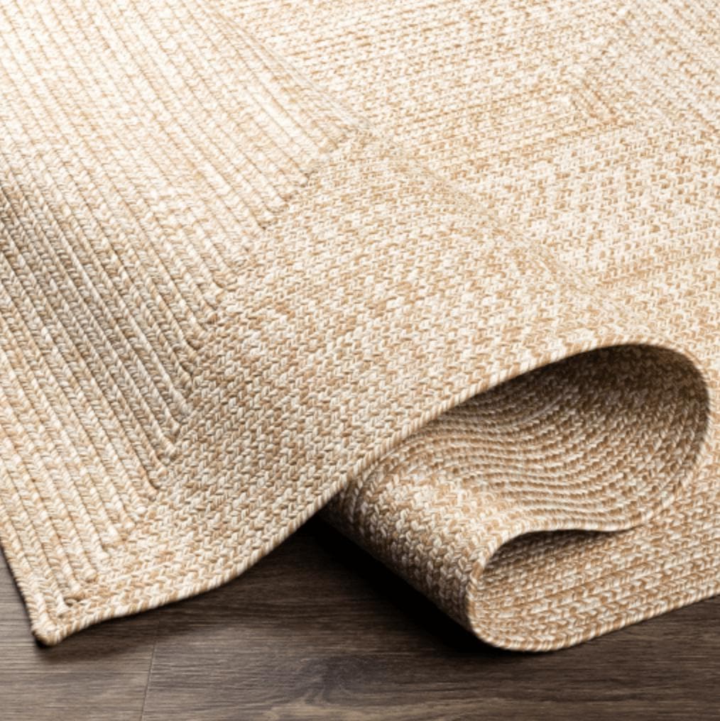 Camel and cream braided polypropylene outdoor rug with a rolled edge on dark wood flooring.