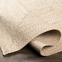 Camel and cream braided polypropylene outdoor rug with a rolled edge on dark wood flooring.