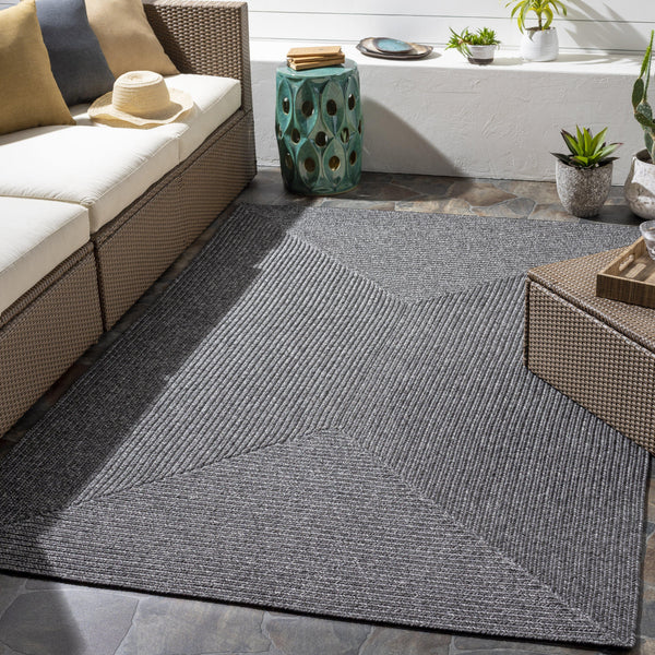 Charcoal gray braided polypropylene outdoor rug with a geometric pattern, enhancing a patio seating area.