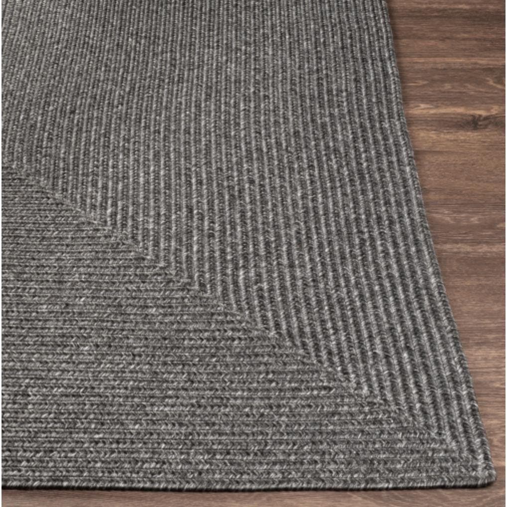 Charcoal gray braided polypropylene outdoor rug with a textured, no-pile surface on a wooden floor.