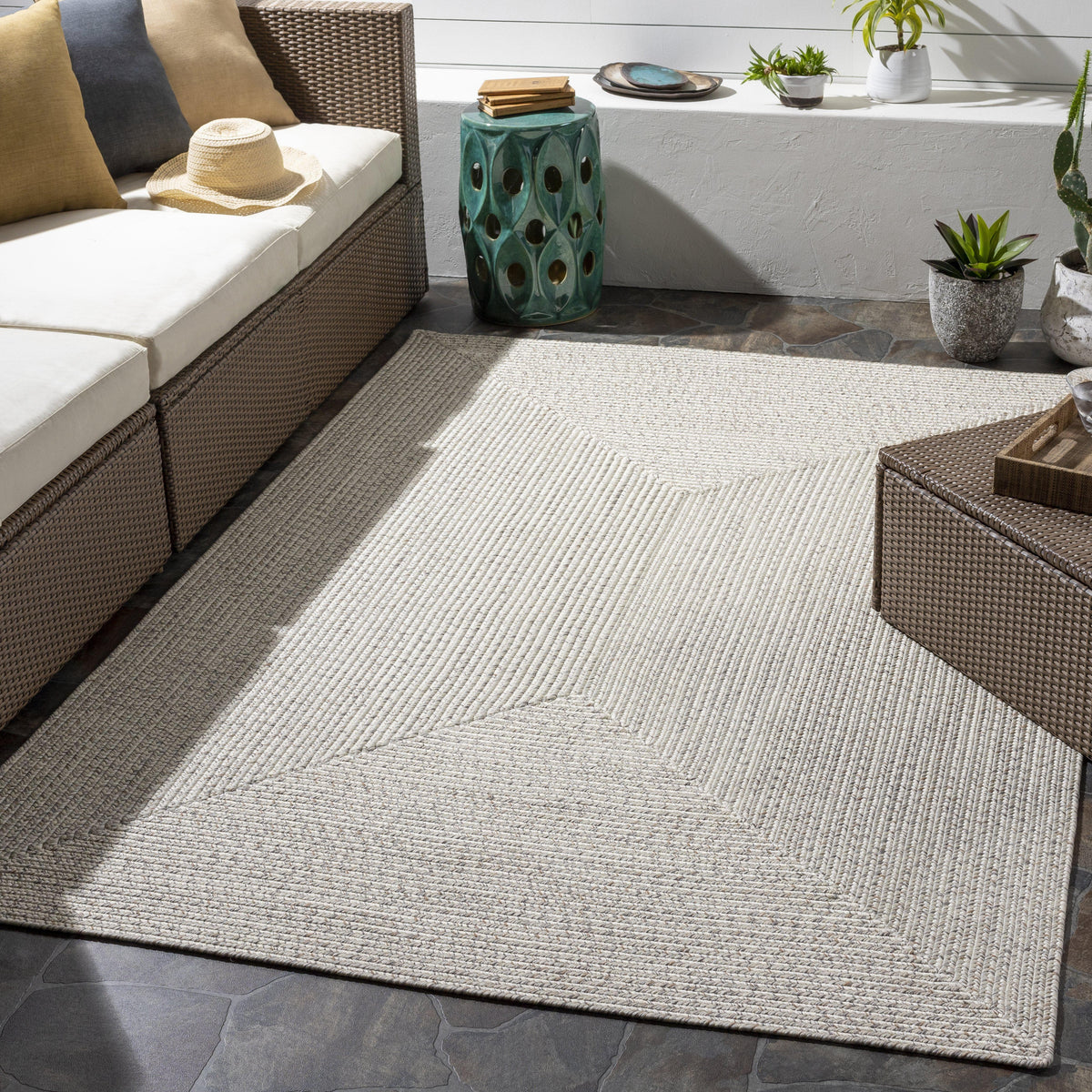 Chesapeake Bay Cream Outdoor Rug, braided polypropylene, no pile, on a patio with wicker furniture.