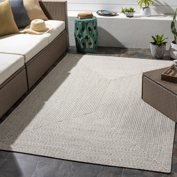 Chesapeake Bay Cream Outdoor Rug, braided polypropylene, no pile, on a patio with wicker furniture.