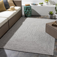 Chesapeake Bay Gray outdoor rug, braided polypropylene, shown on a patio with wicker furniture.