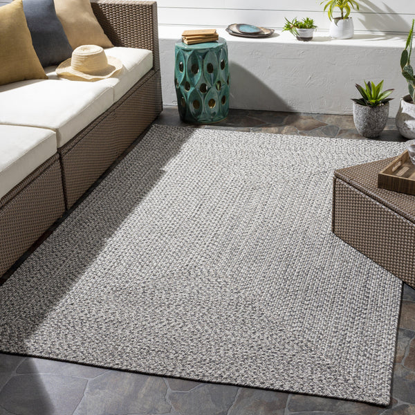 Chesapeake Bay Gray outdoor rug, braided polypropylene, shown on a patio with wicker furniture.