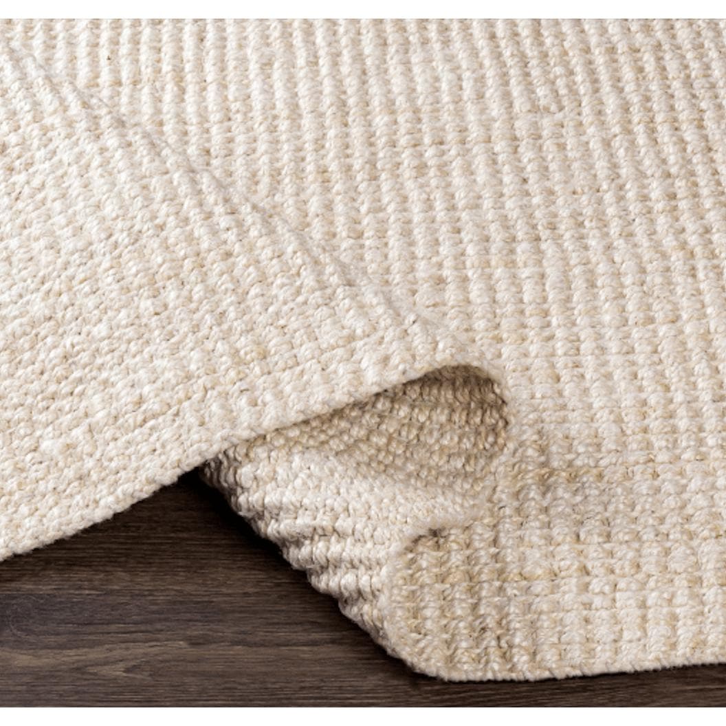Chunky Naturals Cream Jute Rug, hand-woven with a textured, no-pile design, partially rolled on a dark wood floor.
