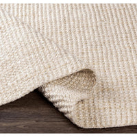 Chunky Naturals Cream Jute Rug, hand-woven with a textured, no-pile design, partially rolled on a dark wood floor.