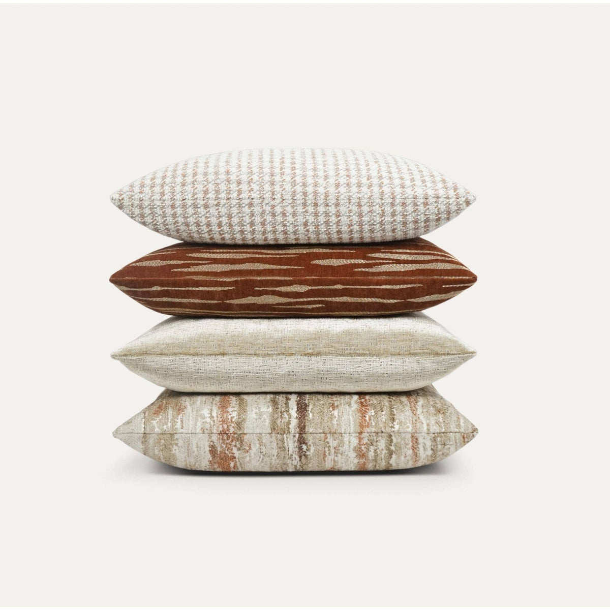 Stack of four luxury designer throw pillows in rust, cream, and beige with varied textures.