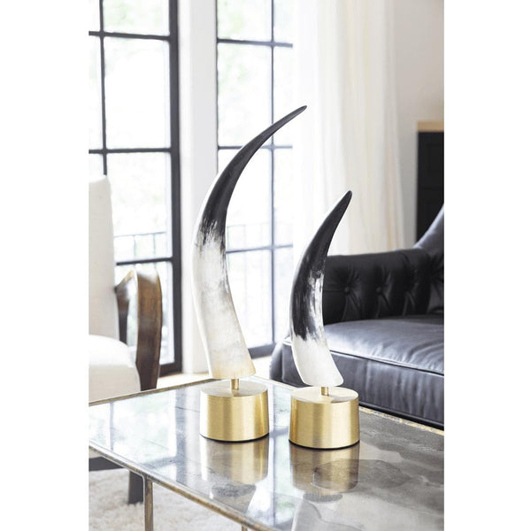 Two black and white natural horn sculptures with matte finish on brass bases, displayed on a glass table.