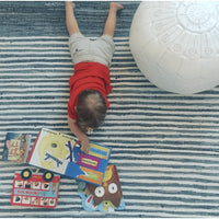Child playing on a blue and white striped denim cotton hand-woven rug next to a white pouf.