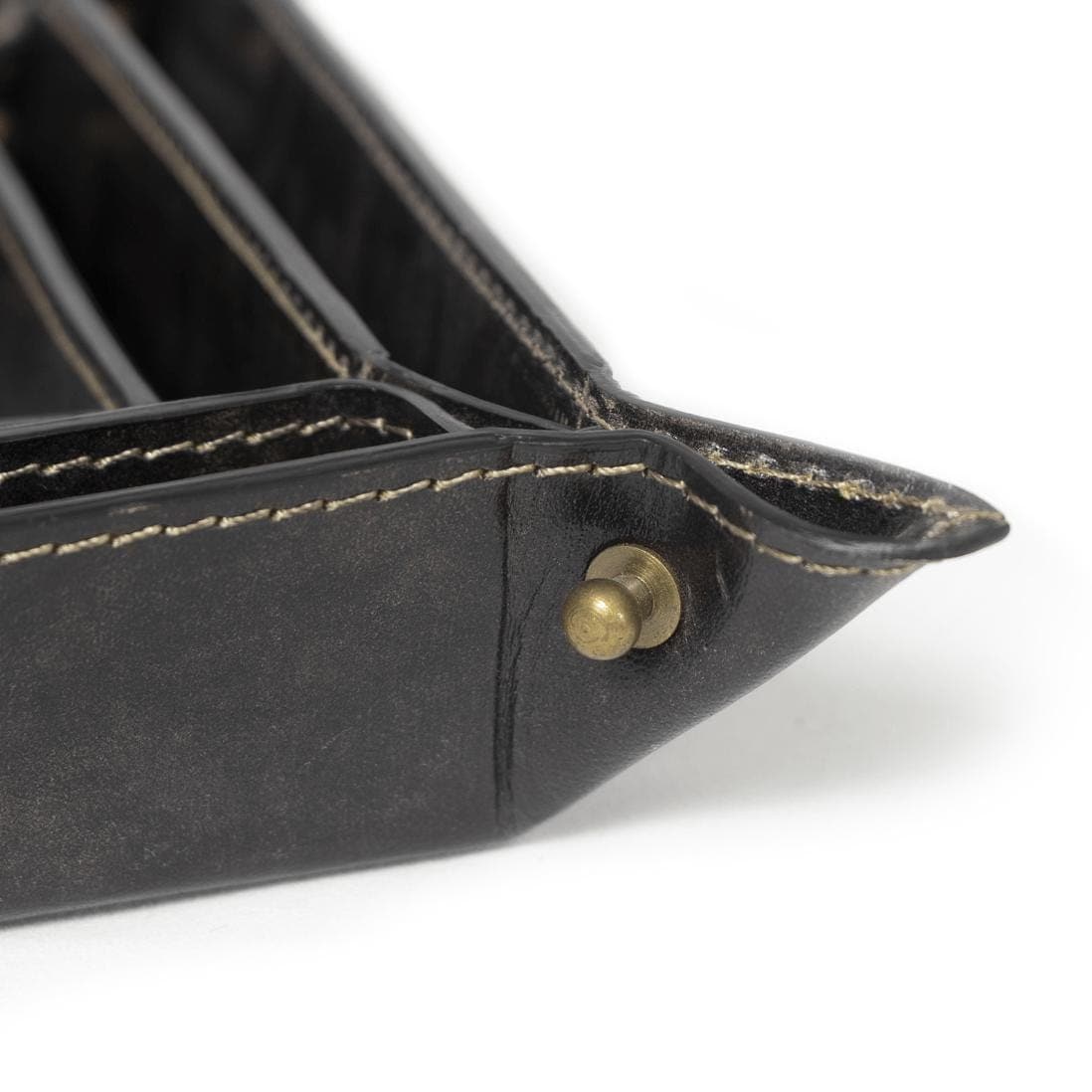 Close-up of a black genuine leather Derby tray with natural brass button snaps and visible stitching.