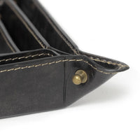Close-up of a black genuine leather Derby tray with natural brass button snaps and visible stitching.