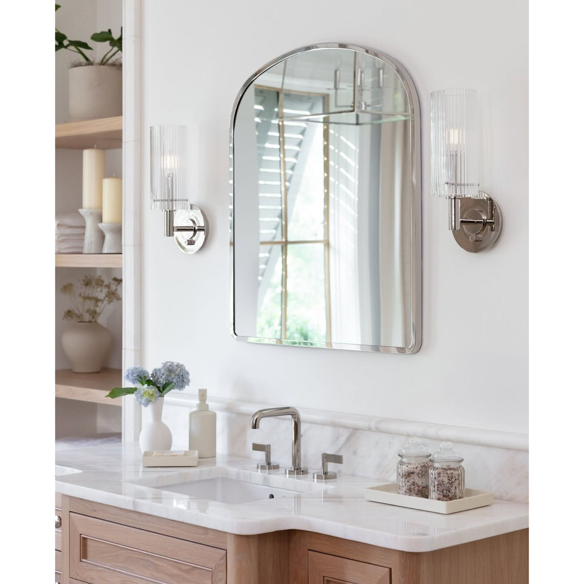 Bathroom vanity with a polished nickel arched mirror, and polished nickel sconces above a sink.