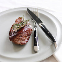 Steak with rosemary on a white plate with a knife and fork.