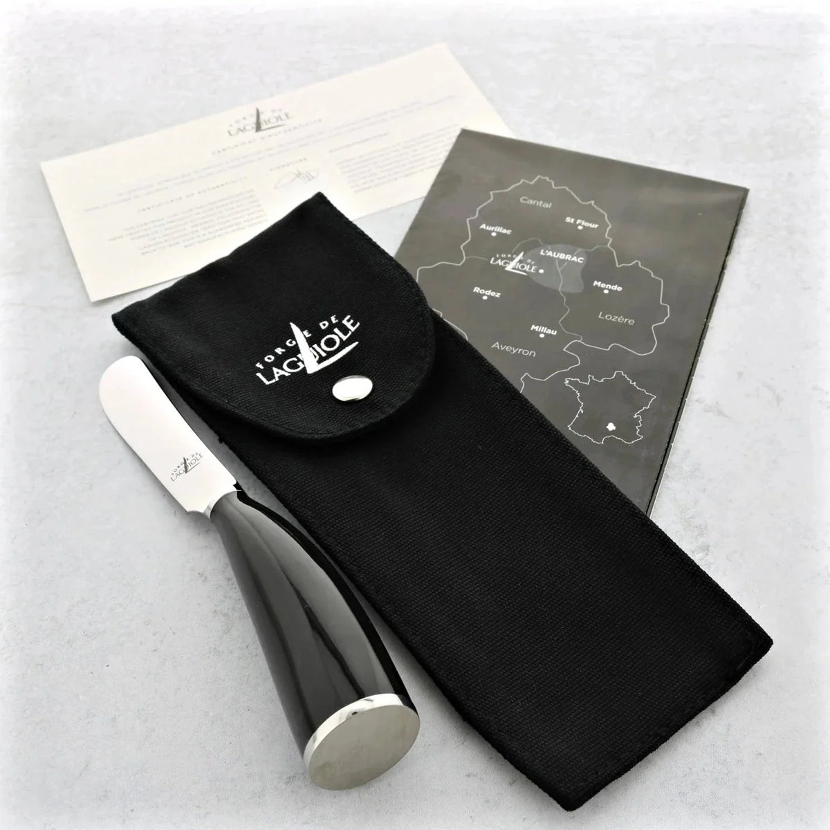 Cheese knife with black handle and silver blade, accompanied by a black pouch and a map on a light gray background.