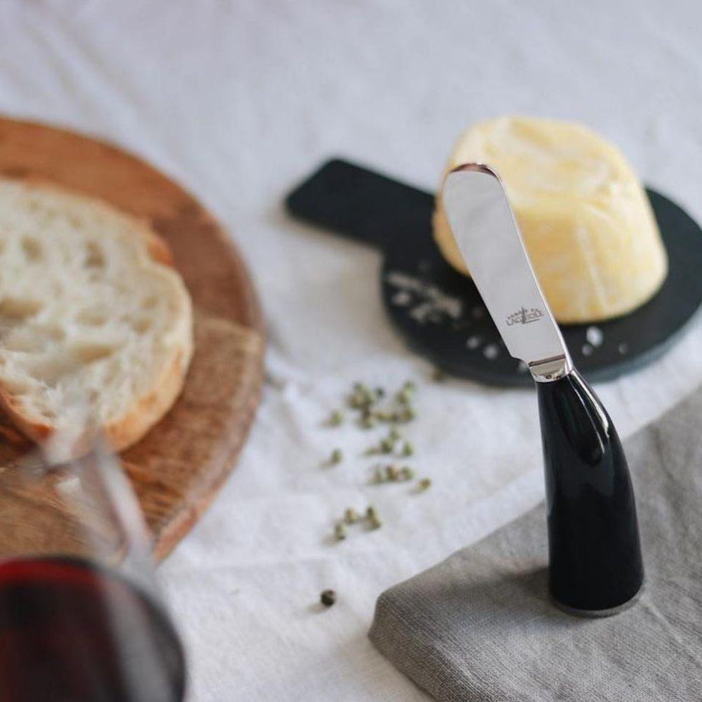 Butter knife with a black handle on a stone surface next to bread and a glass of red wine.