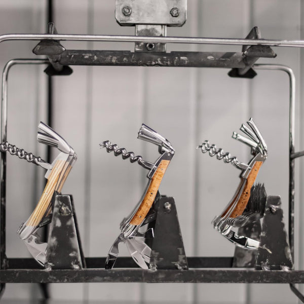 Three corkscrews with wooden handles on a metal stand against a neutral background