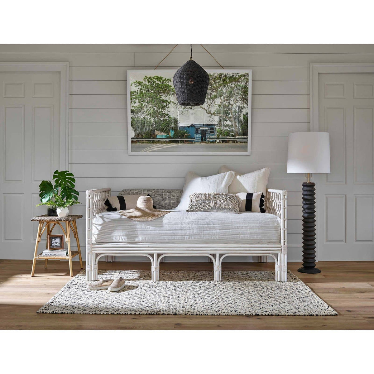 Black rattan Georgian pendant light with natural brass accents, hanging over a daybed in a coastal-style room.