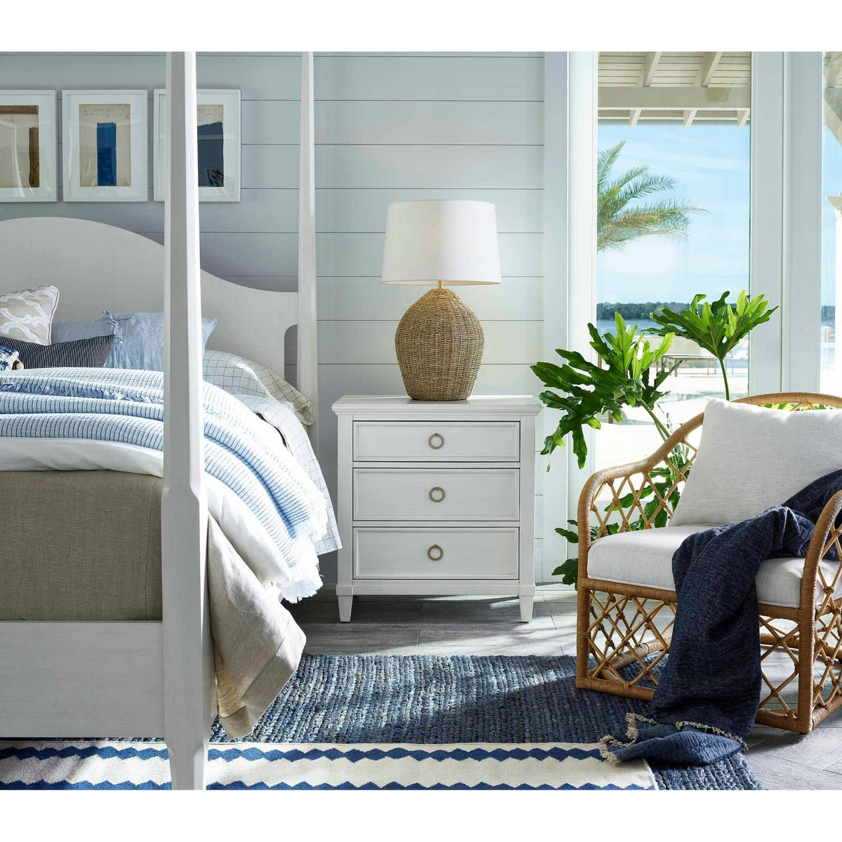 Georgian table lamp with natural rattan base and linen shade on a white nightstand in a coastal bedroom.