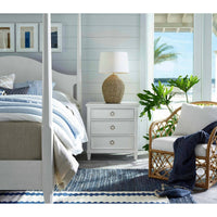 Georgian table lamp with natural rattan base and linen shade on a white nightstand in a coastal bedroom.