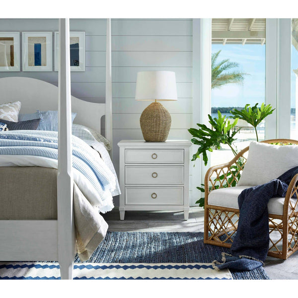 Georgian table lamp with natural rattan base and linen shade on a white nightstand in a coastal bedroom.
