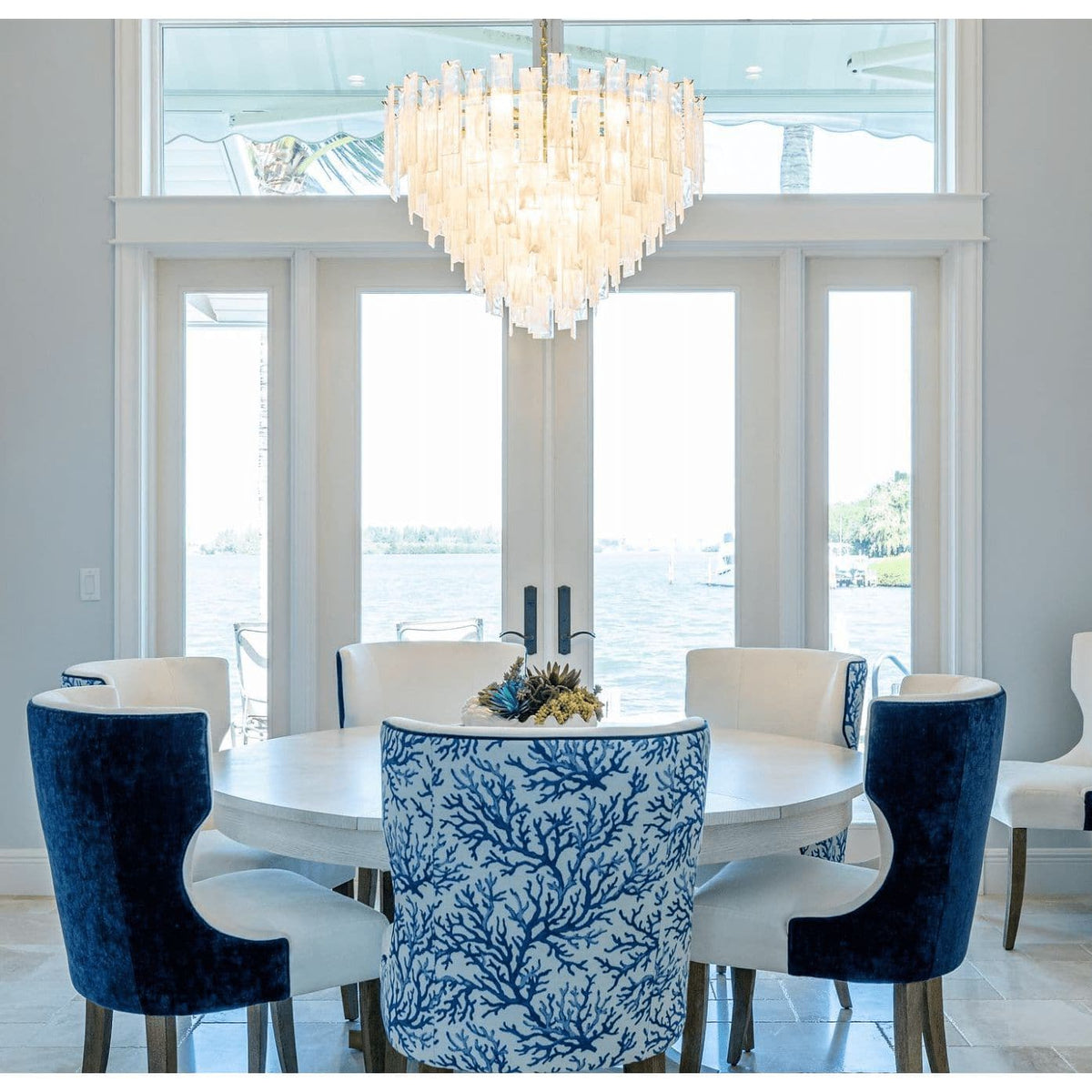 Glacier Glass & Brass Chandelier with striking water glass panes and white swirls, hanging above a dining table.